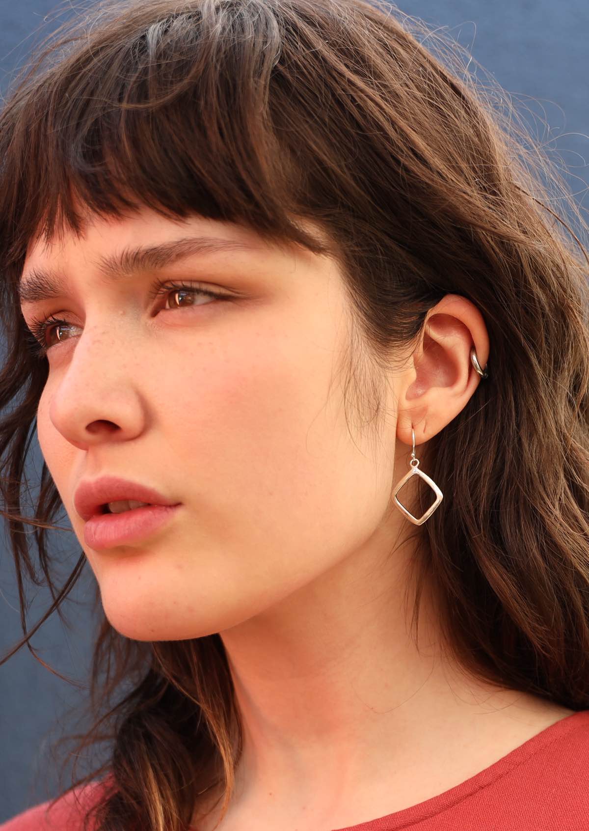 Model with dark hair wearing geometric shaped dangly silver earrings