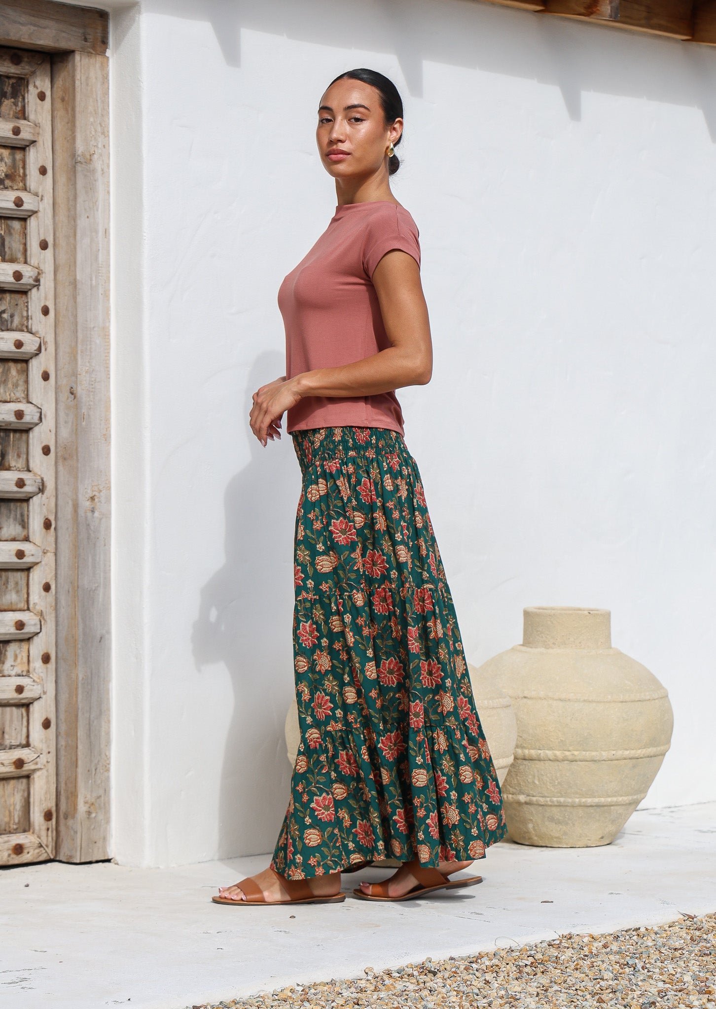 Model standing sideways wears a cotton maxi skirt with wide elasticated waistband in deep green based floral print.