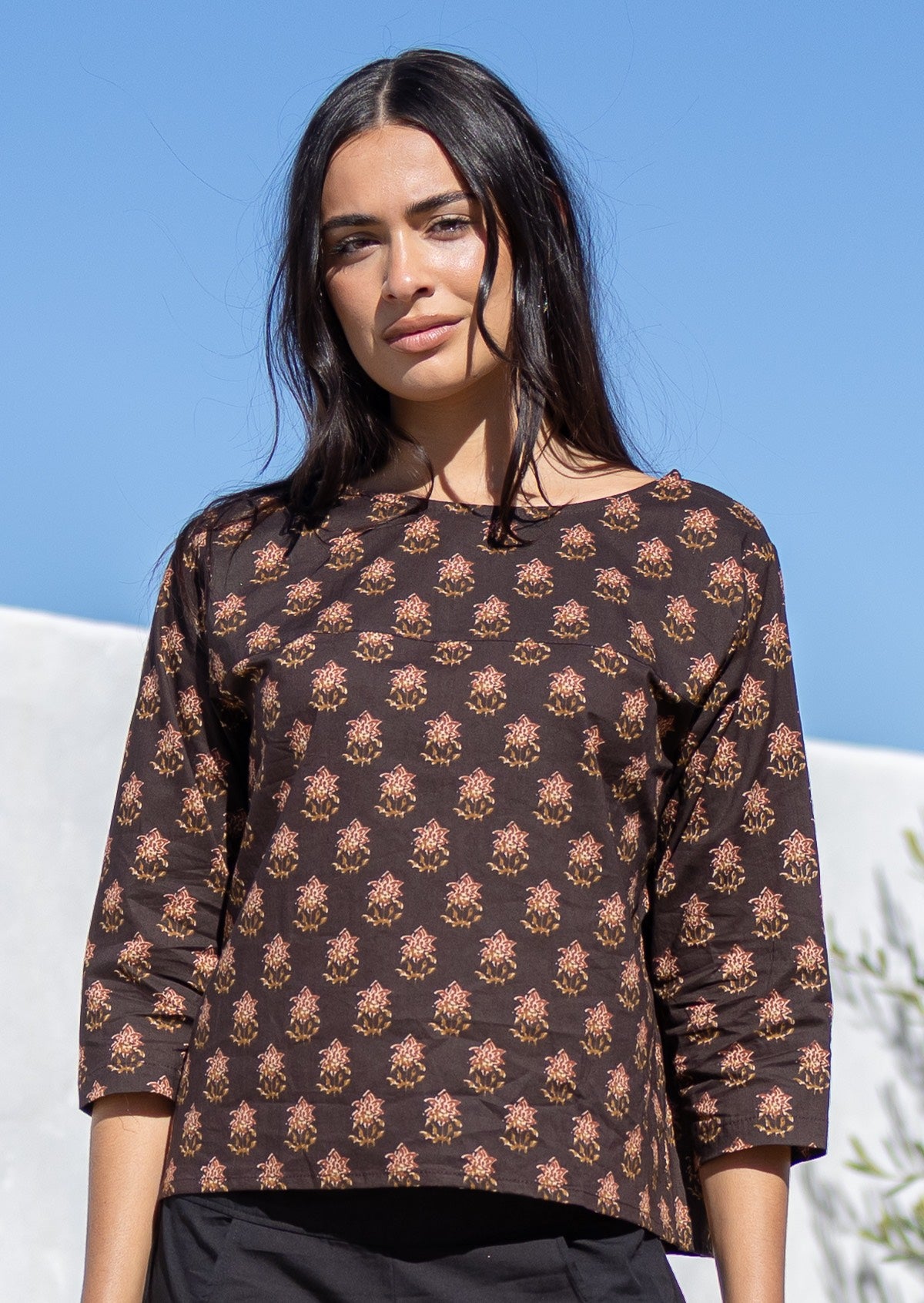 Woman wearing a loose, brown, Indian cotton patterned top against a blue sky