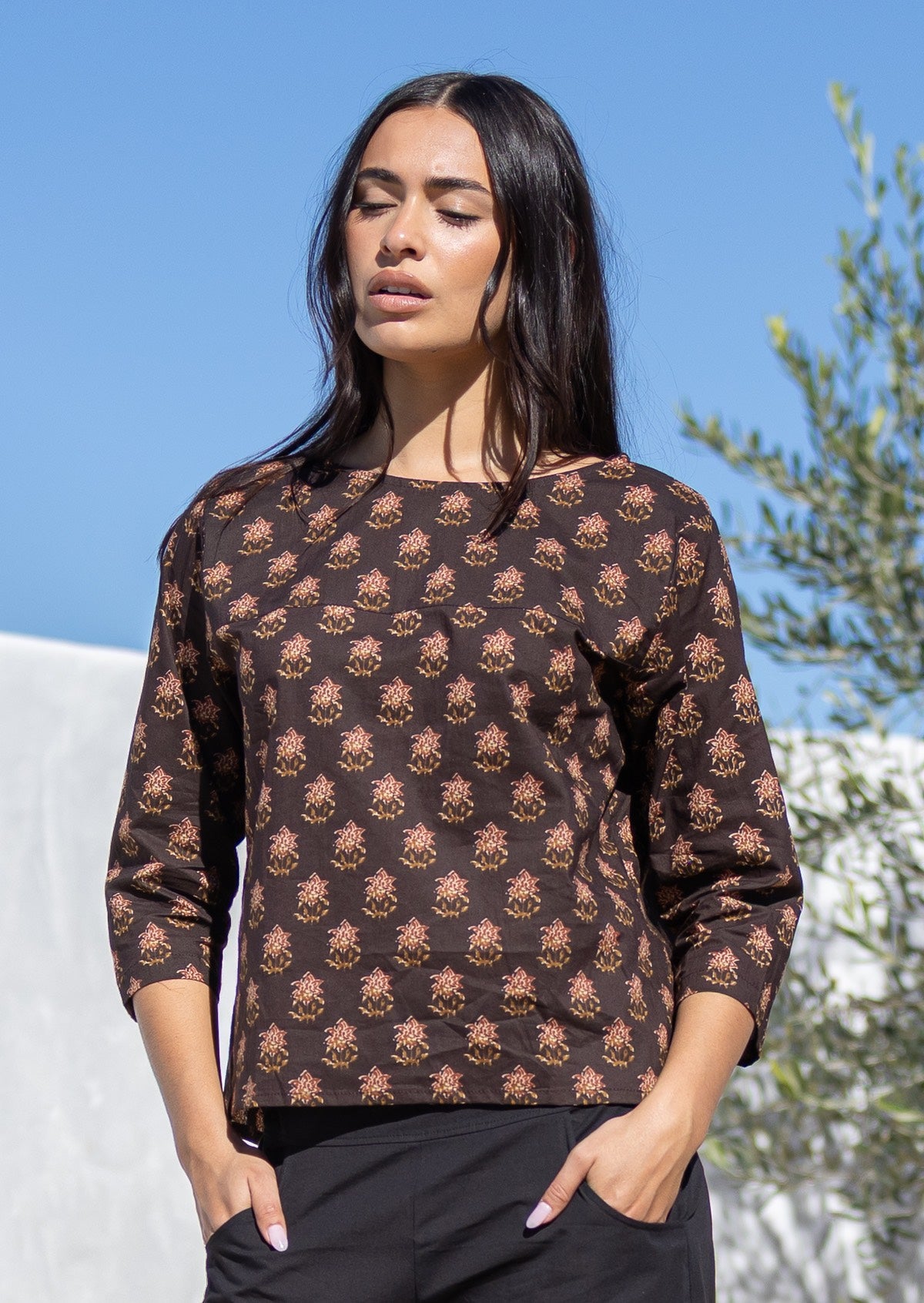 Woman wearing a brown Indian cotton patterned top with a clear blue sky and greenery in the background