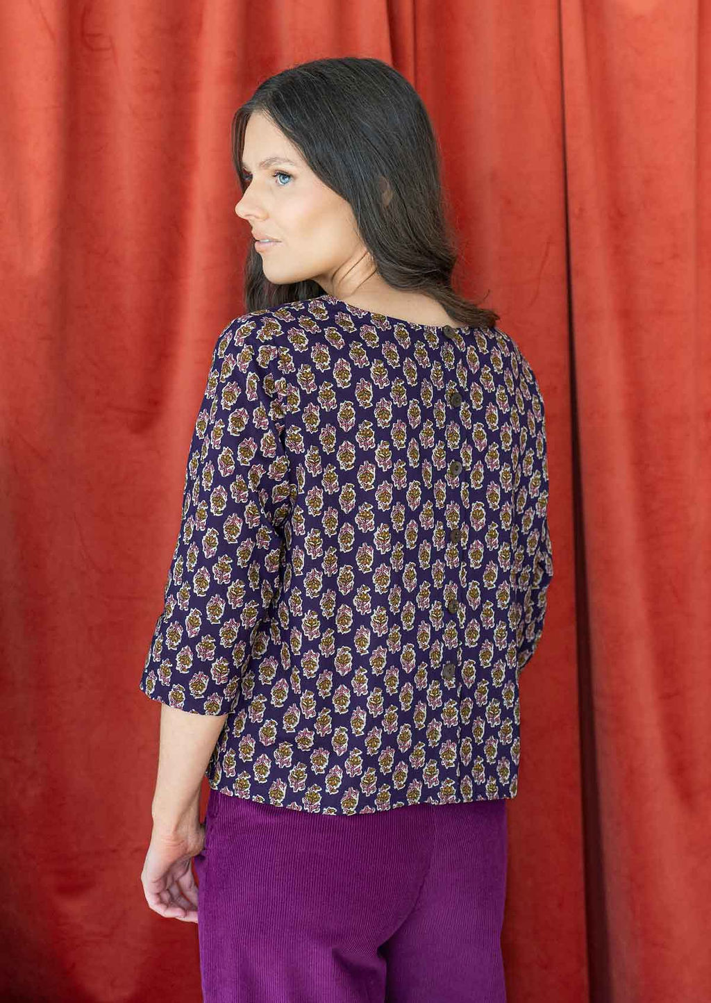 Model wearing a boxy fit cotton top with 3/4 sleeves, round neckline and decorative buttons at the back.