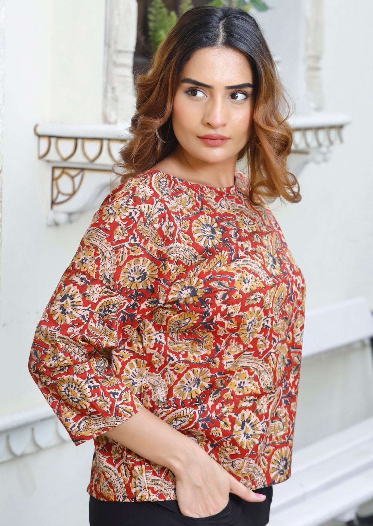 Model wears loose fit cotton top in warm toned floral pattern on red base.