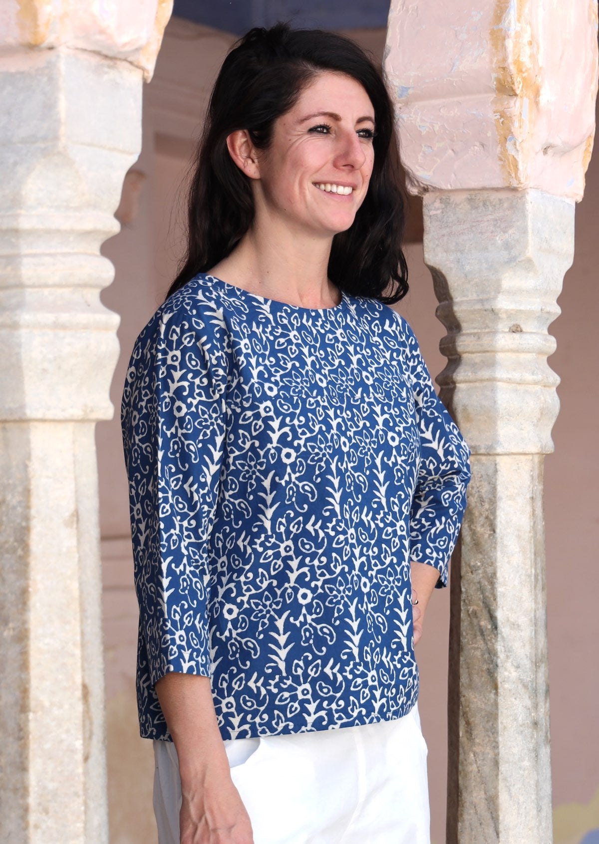 Woman stands sideways in cotton loose fit top with 3/4 sleeves and round neckline