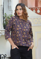 Woman wears cotton lose fit top in pink, cream and light brown floral print on dark purple base.