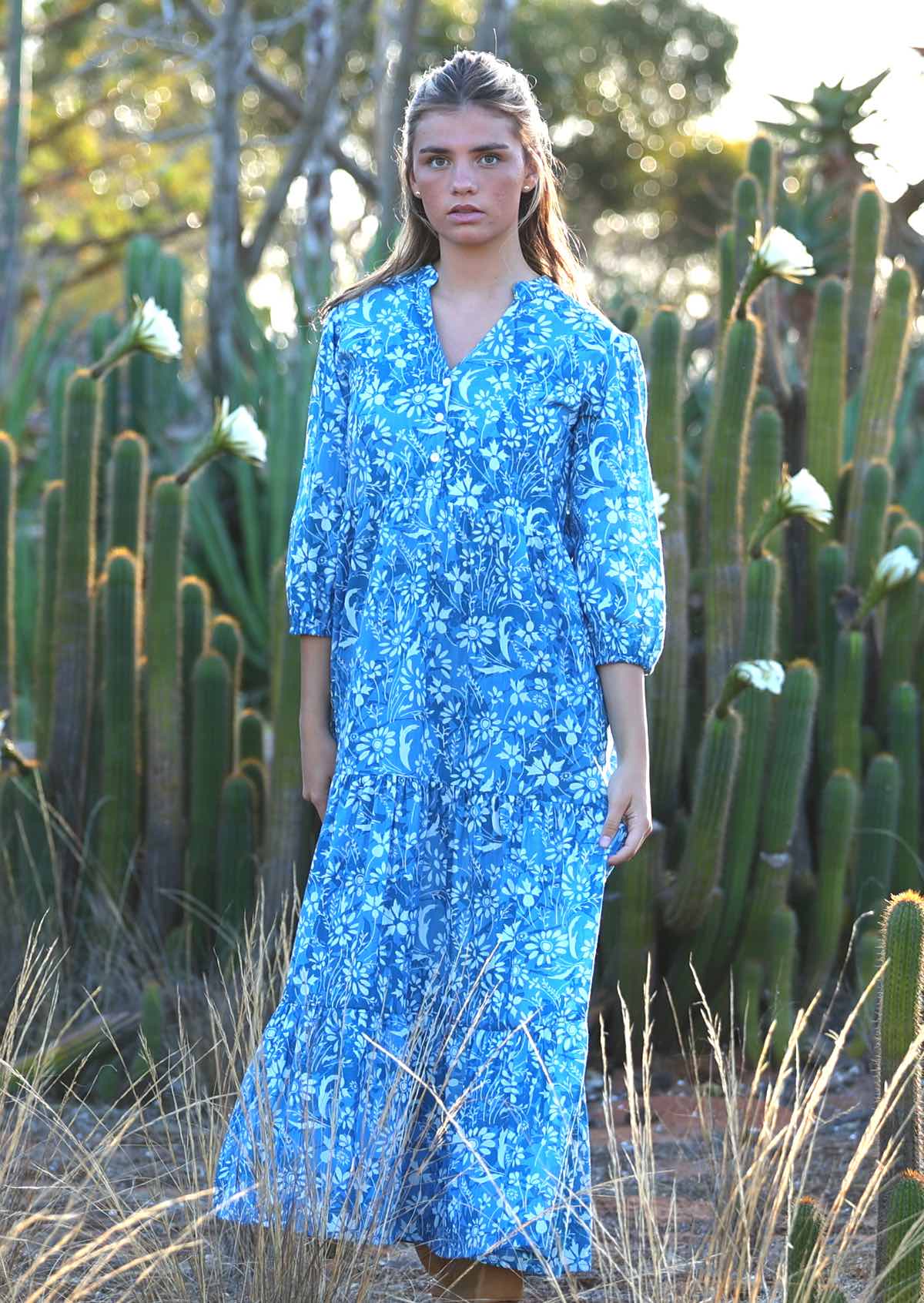 woman in blue cotton maxi dress with light blue and white floral print in front of cactus