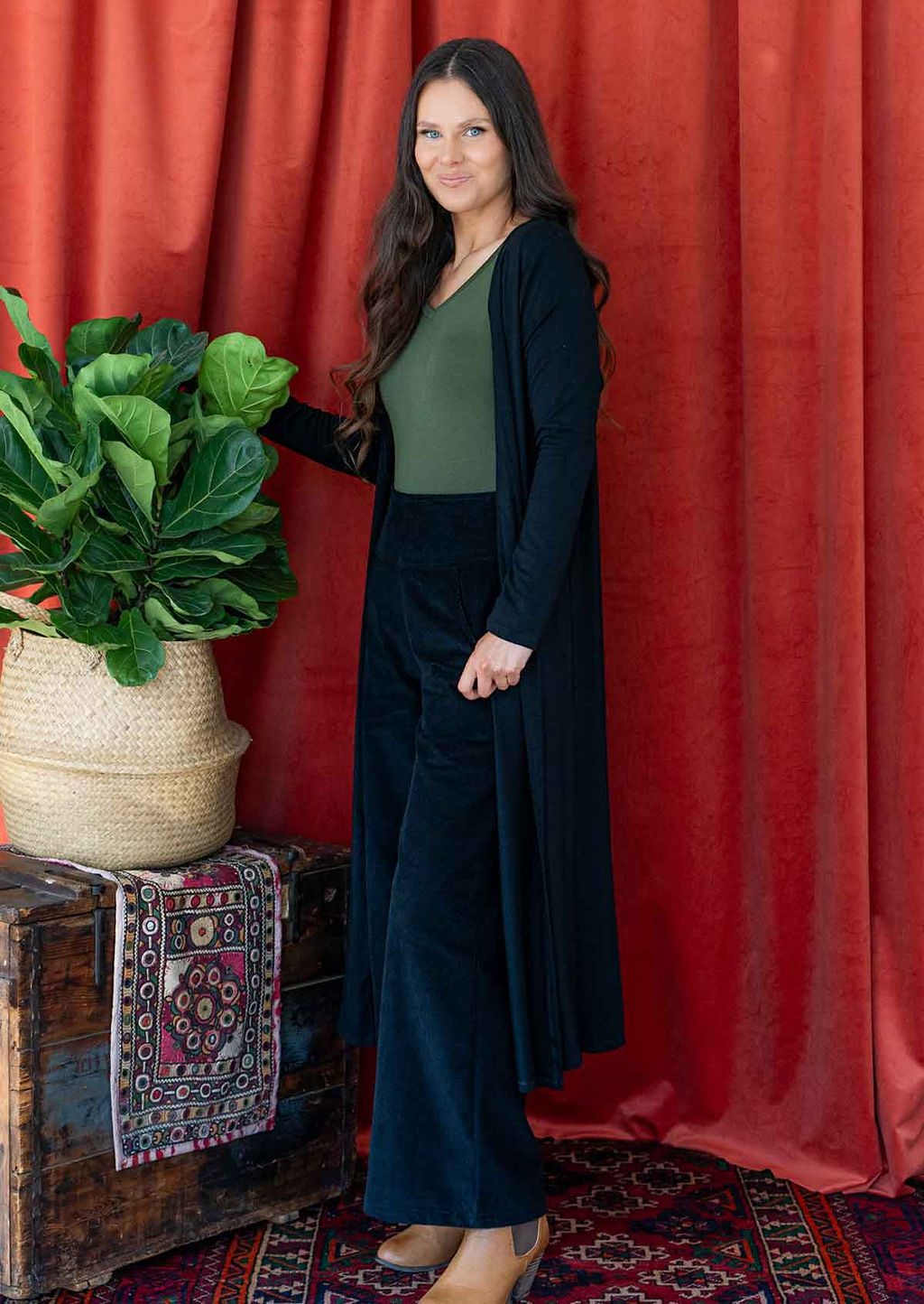 Woman wearing long black jersey duster jacket over black corduroy pants and green top