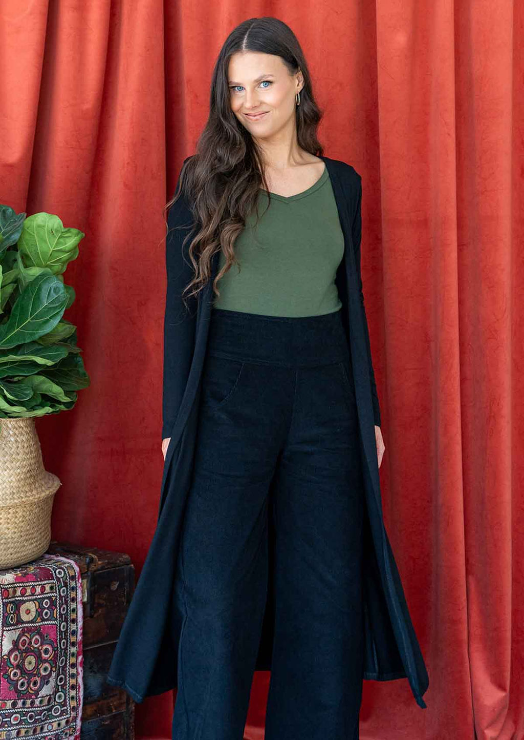 Woman wearing long black jersey duster jacket over black corduroy pants and green v-neck top