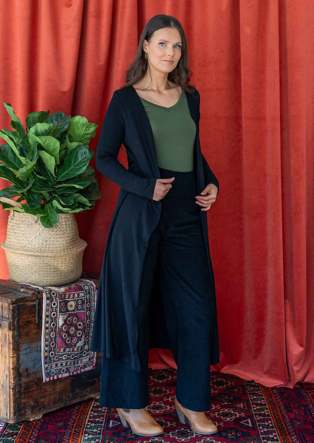 Woman wearing long black stretch jersey duster jacket over corduroy pants and green v-neck top