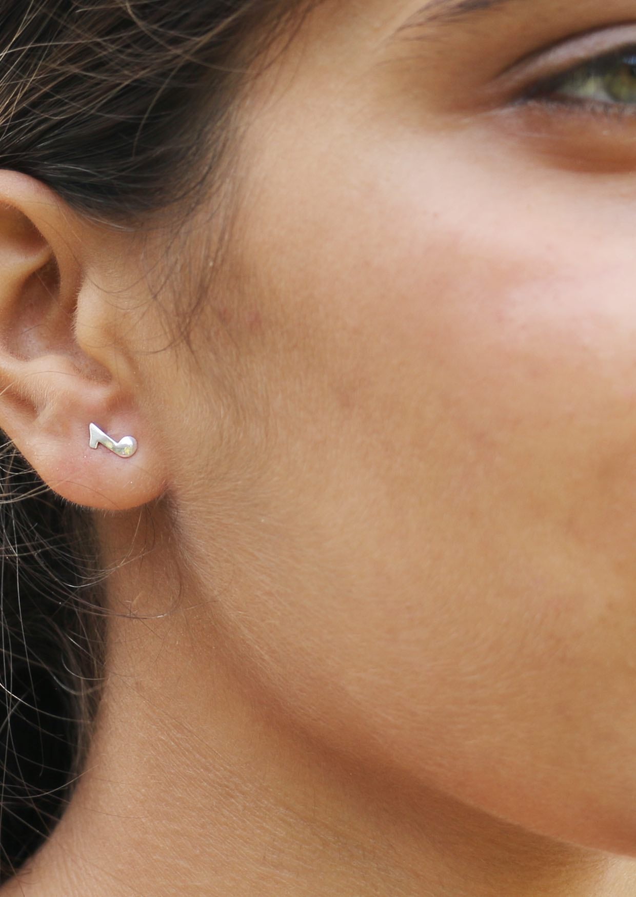 Close-up of a person wearing a musical eight note sterling silver studs with butterfly backs