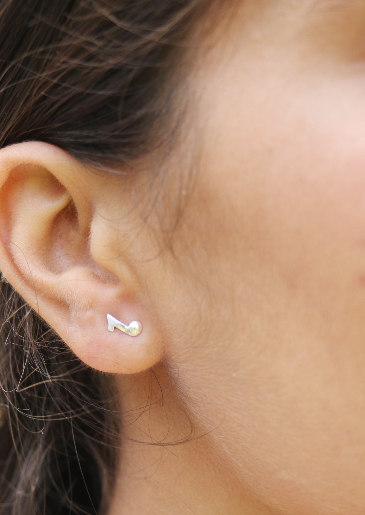 Close-up of an ear wearing a small silver quaver, eighth note stud earrings with secure butterfly backs