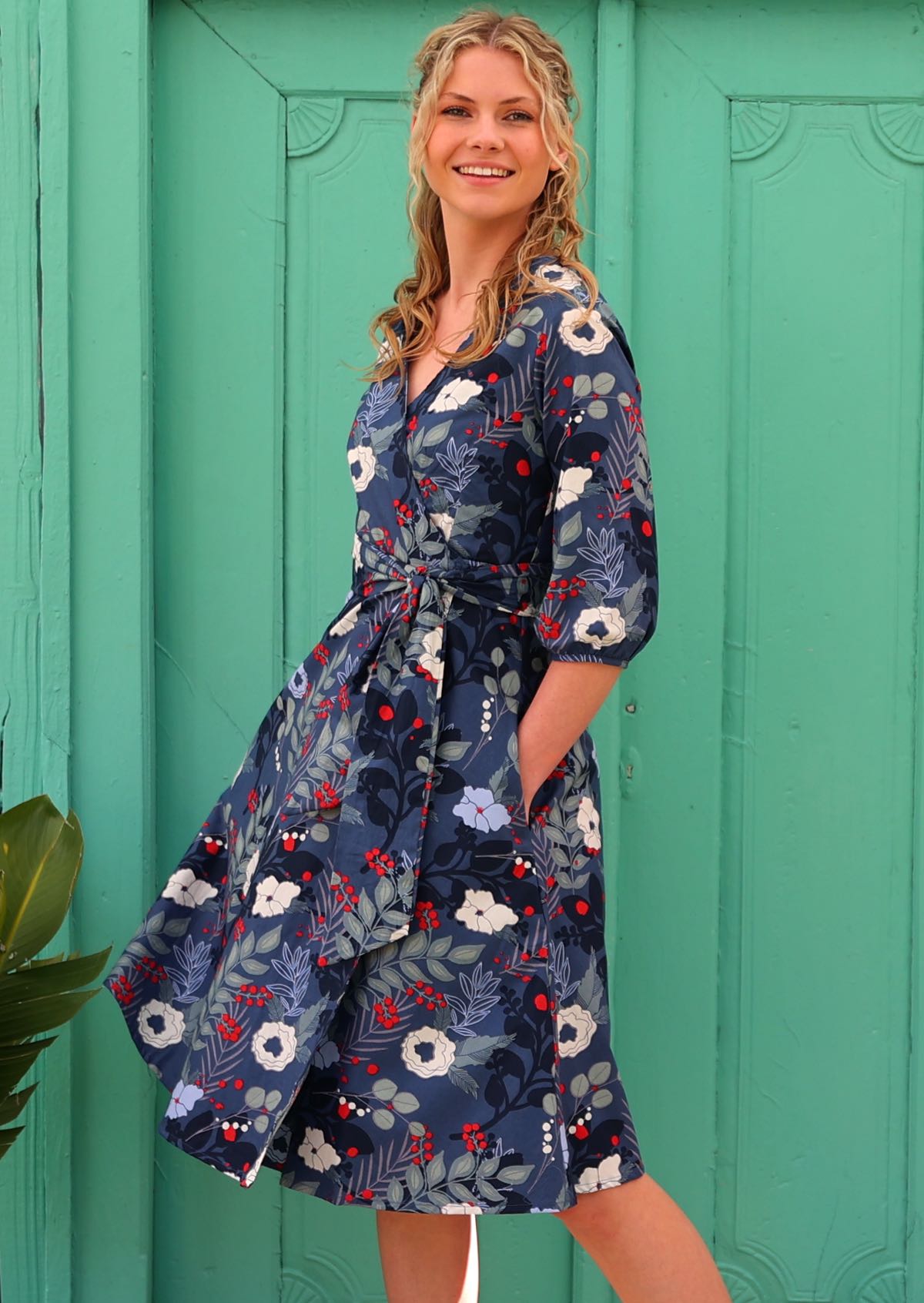 woman in 100% cotton wrap dress in blue with white flowers and long sleeves in front of aqua door