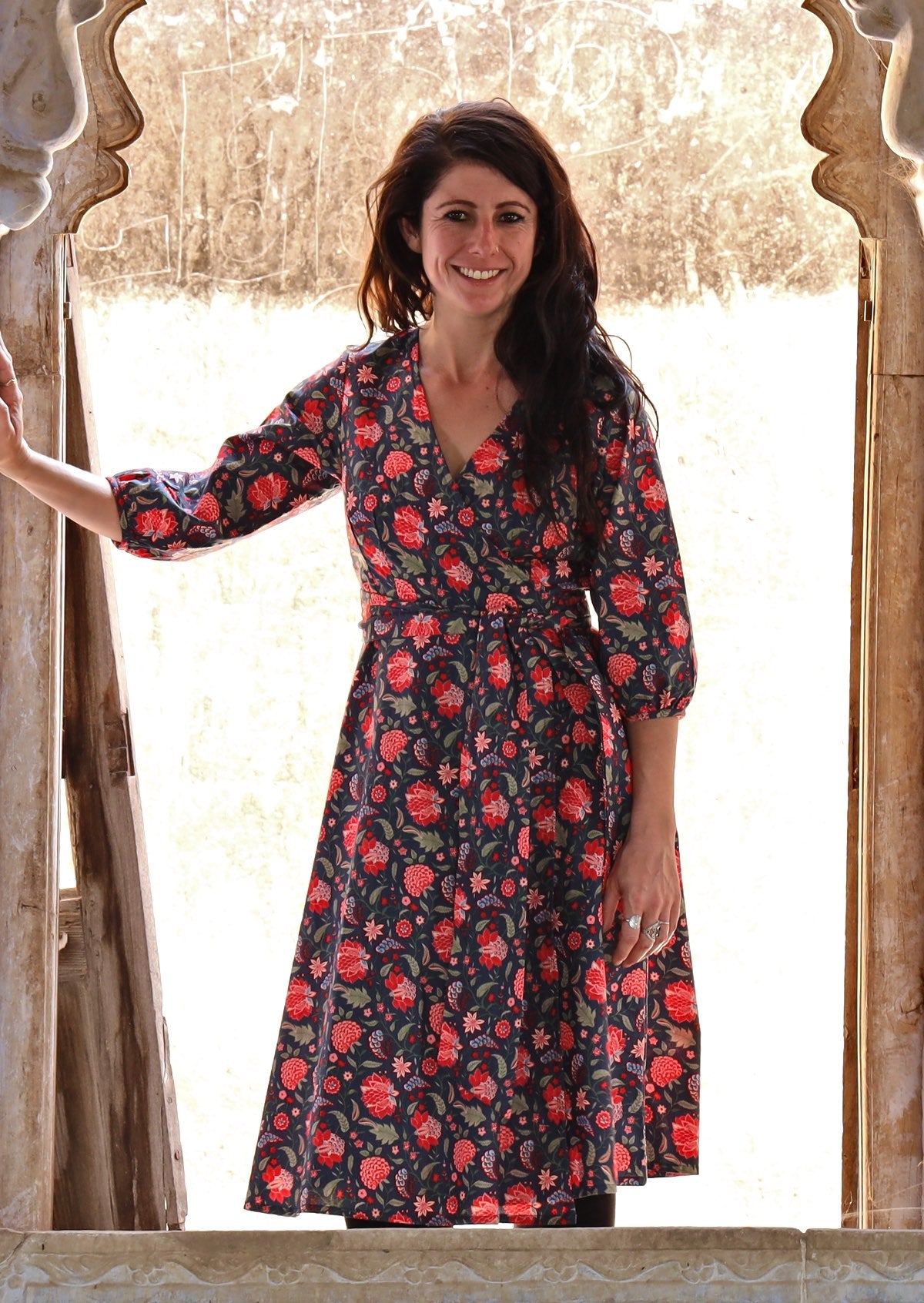 Model posing in over the knee length wrap dress with flowing skirt and formation of V neckline.
