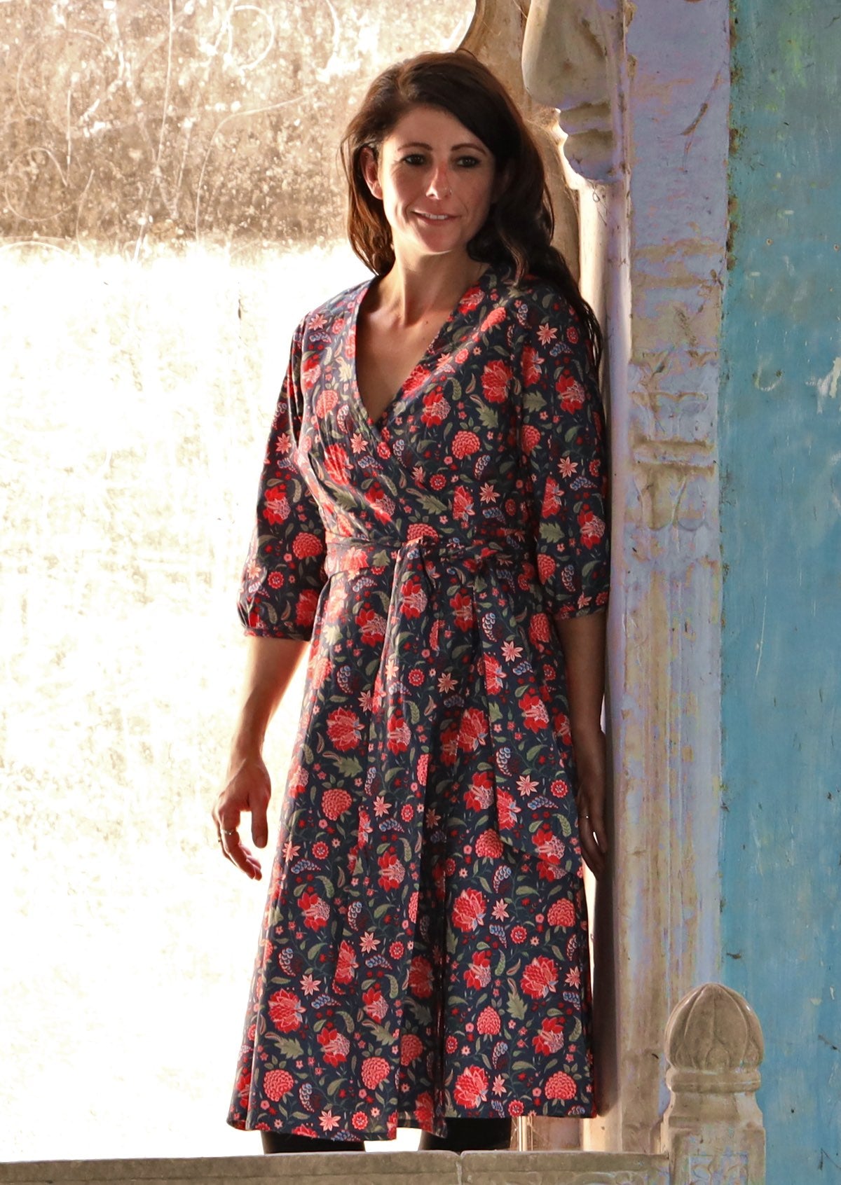 Model wearing navy blue based cotton wrap dress with printed bright red florals and 3/4 sleeves.