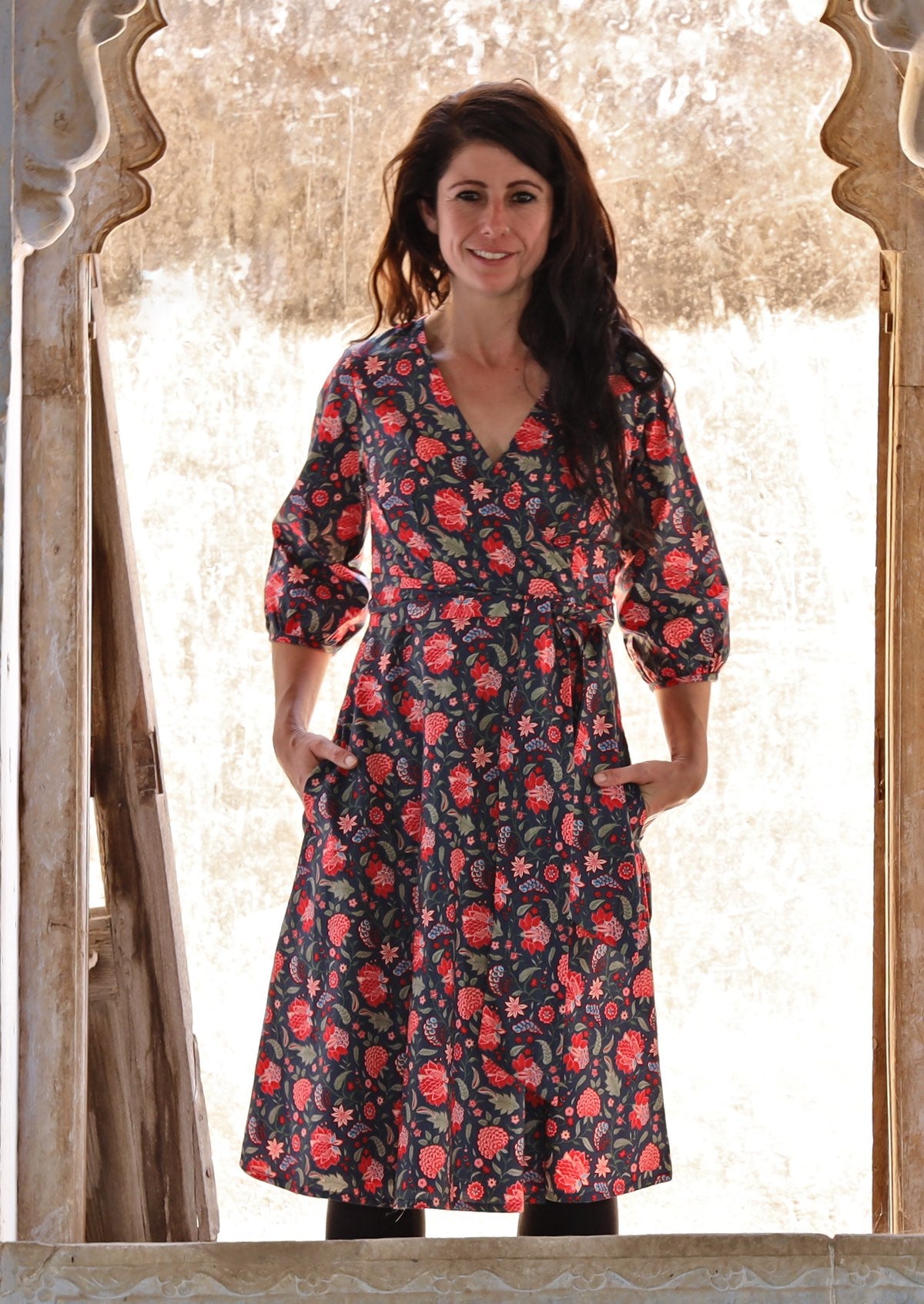 Woman standing with both the hands in pockets of a beautiful cotton ella wrap dress in bright floral print.