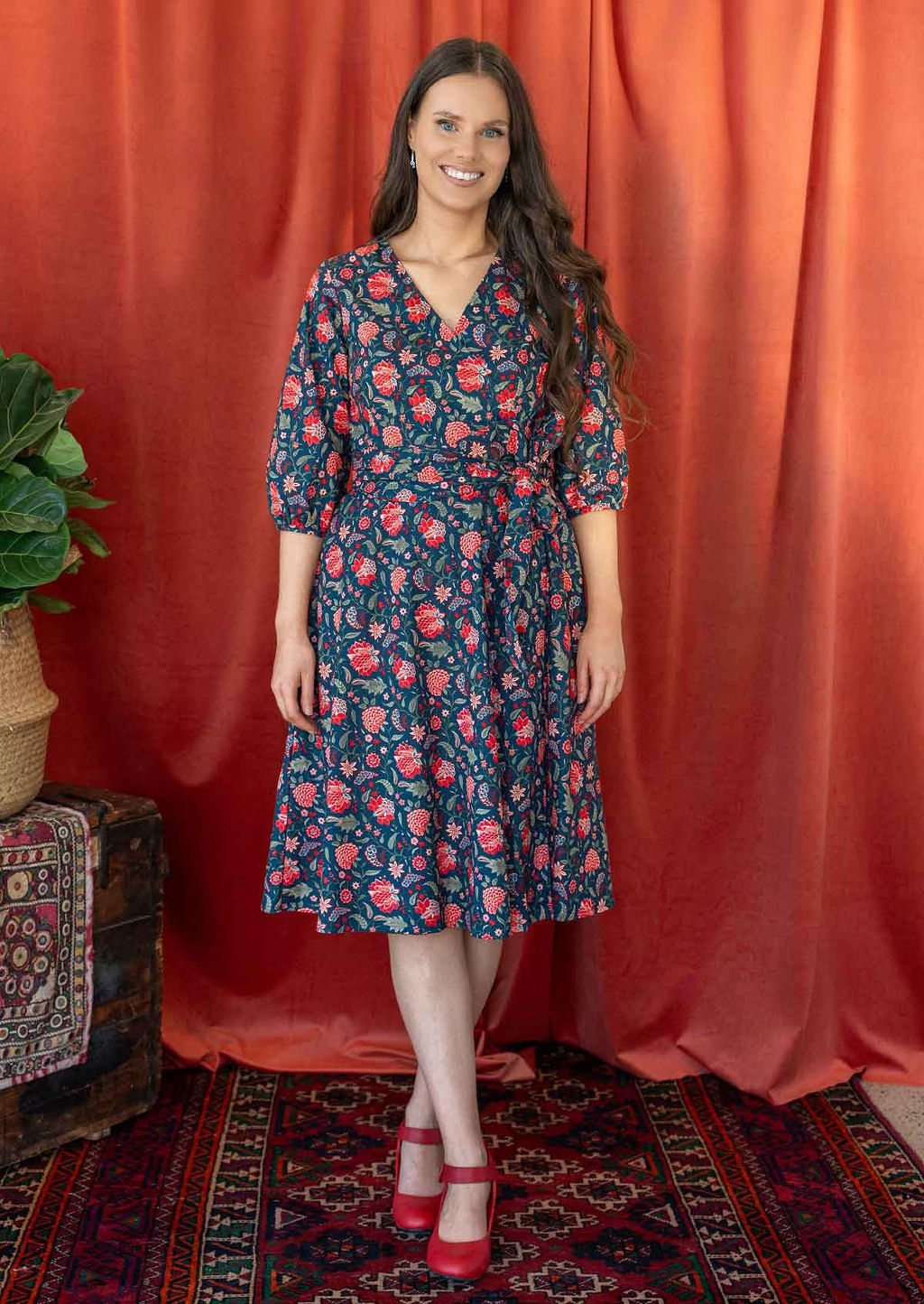 Model wears a blue based floral printed cotton wrap dress with V-neckline, 3/4 sleeves, a wide waist-tie and pockets