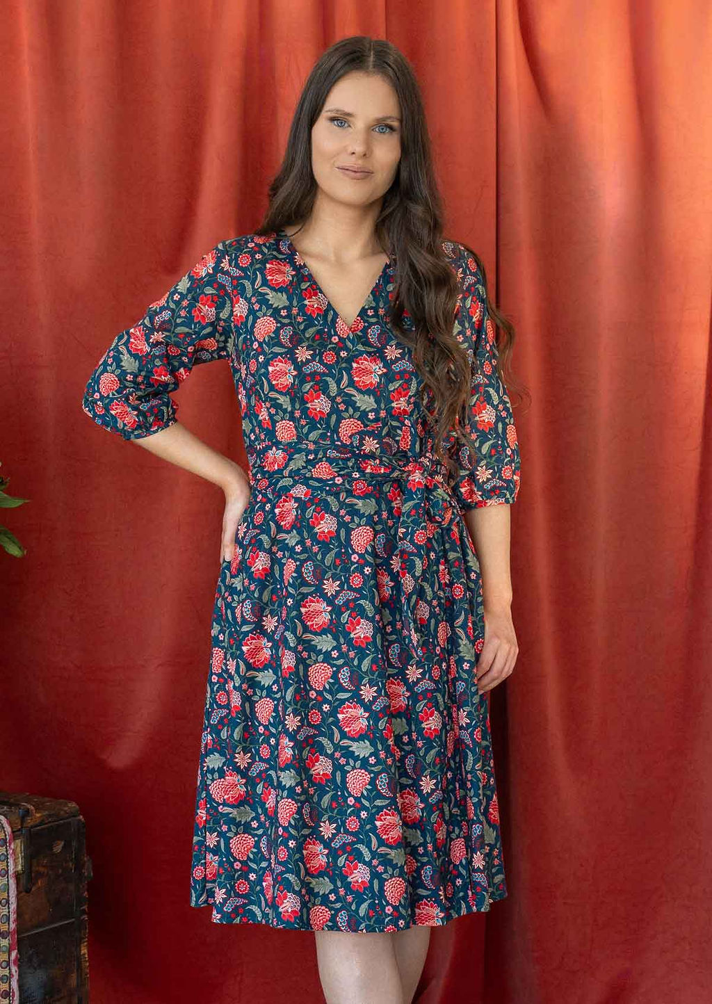 Model wears a blue based floral printed cotton, over the knee length wrap dress with V-neckline, 3/4 sleeves, and a wide waist-tie