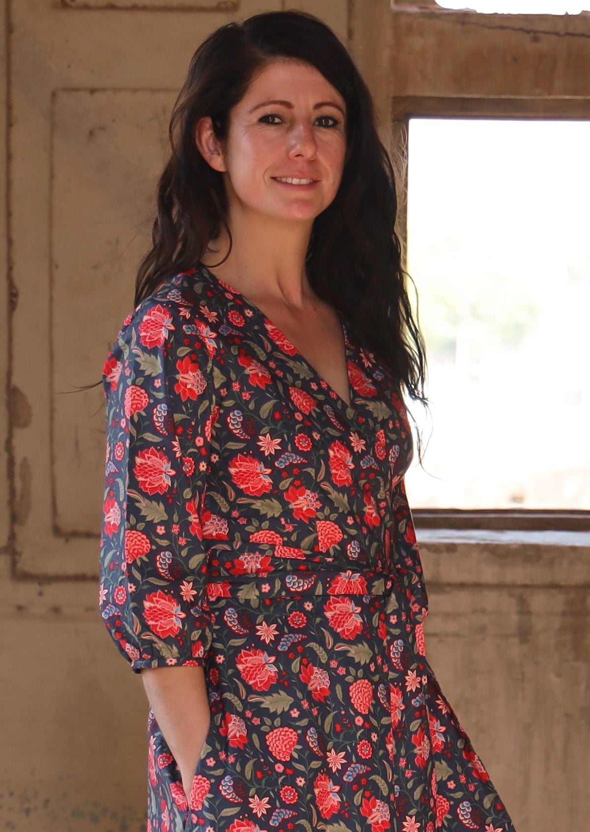 Close up of a model wearing a gorgeous floral printed wrap dress in shades of green, red, peach and navy blue.
