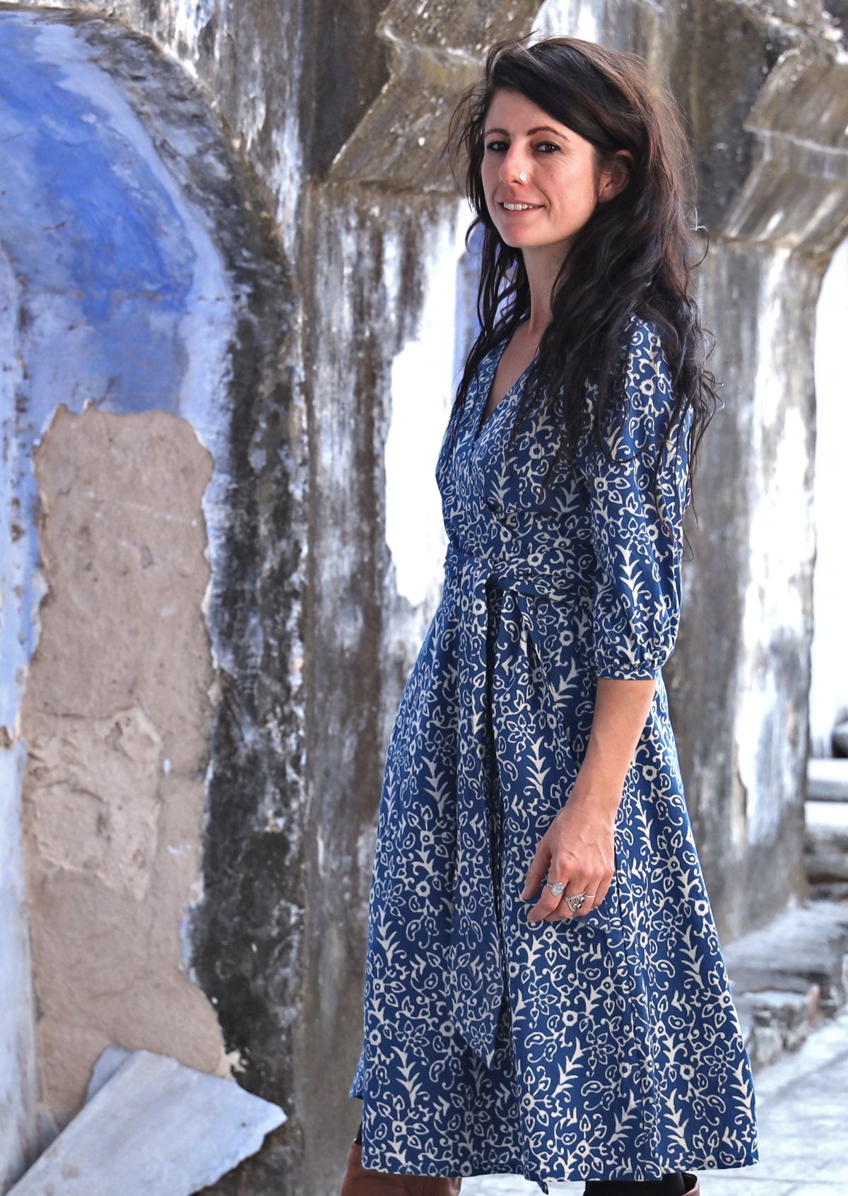 Model wearing blue based cotton wrap dress with white floral print and 3/4 sleeves