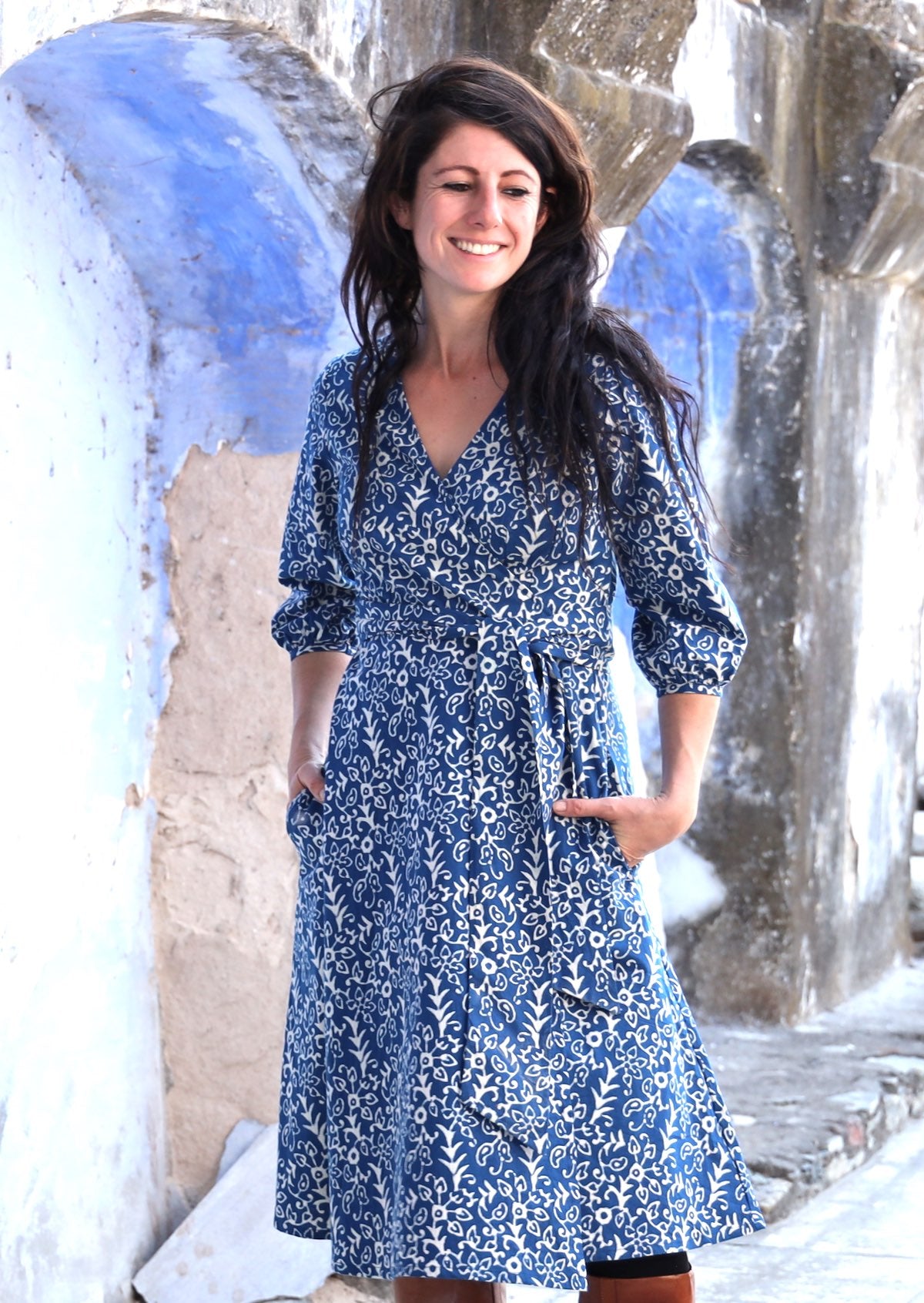 Model wearing 100% cotton dress in a blue base with white floral print. with her hands in side pockets