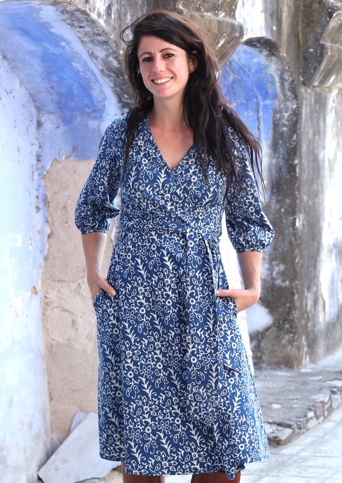 Front pose of model wearing over the knee length wrap dress in blue based cotton print