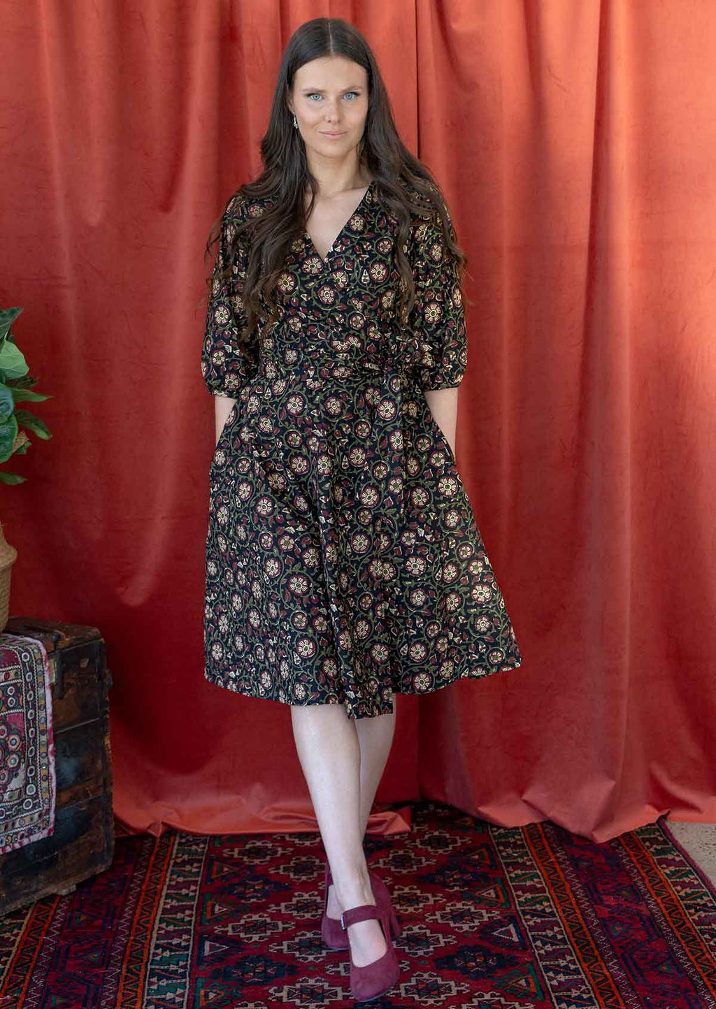 Model wears a black based floral printed cotton wrap dress with V-neckline, 3/4 sleeves, a wide waist-tie and pockets