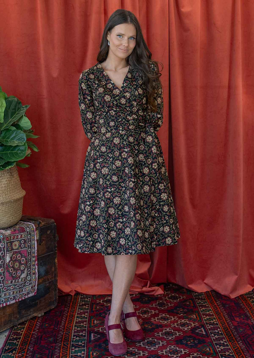 Model wears a midlength cotton wrap dress in black based maroon, cream and olive floral print.