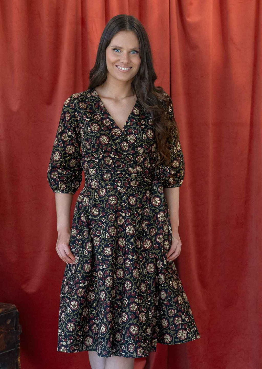 Model standing in a beautiful cotton warp dress with V neckline, 3/4 sleeves, a wide waistband and hands in pockets.