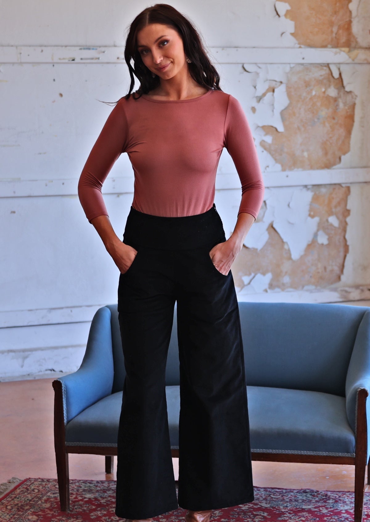 Woman wearing black corduroy wide legged pants with long sleeve pink top with hands in pockets