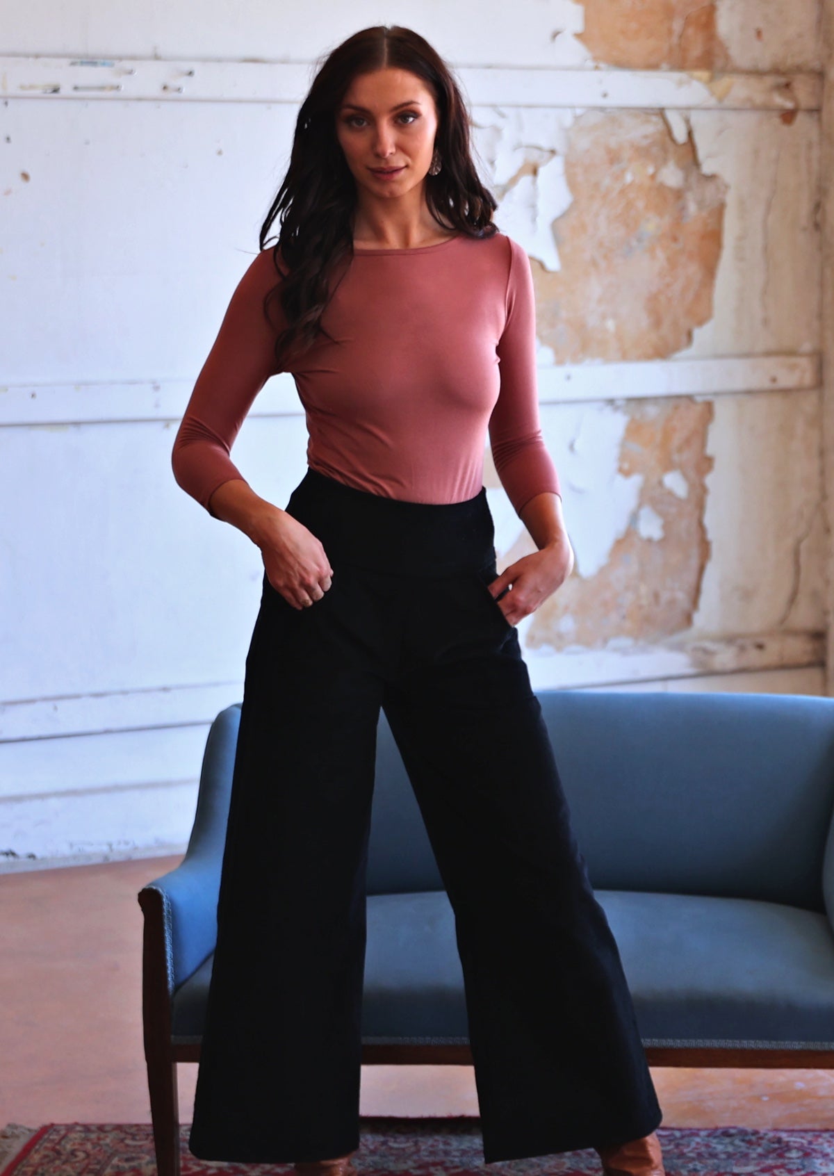 Woman wearing black corduroy wide legged pants with long sleeve boat neck pink top with hands in pockets