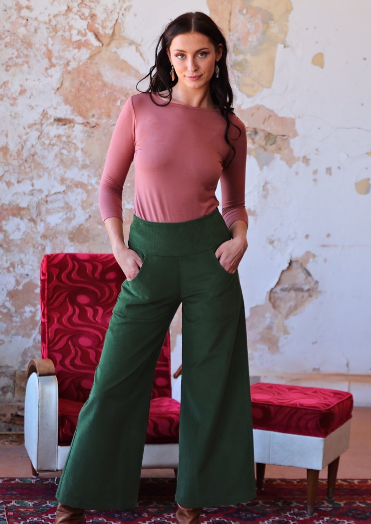 woman wearing long sleeve pink boat neck top and green corduroy pants with hands in pockets