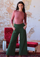 woman wearing long sleeve pink boat neck top and green corduroy pants with hands in pockets