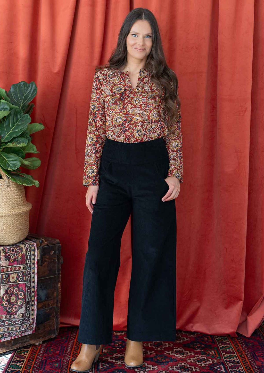 woman wearing black corduroy wide leg pants with hand on hip, paired with printed cotton blouse and ankle boots