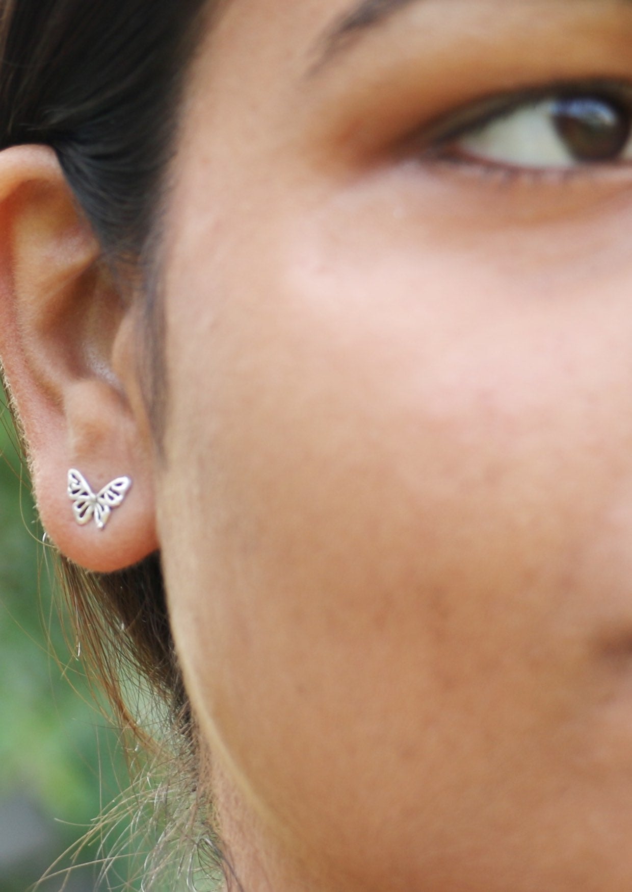 Close up of a person wearing a butterfly-shaped silver stud earring with a blurred background