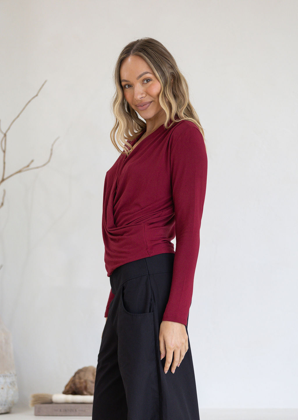 Woman wearing a maroon long-sleeve crossover top and black pants against a light background