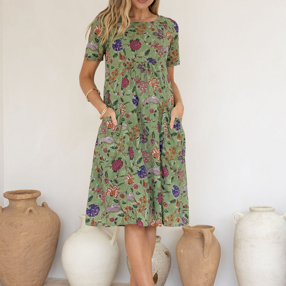 Woman wearing a green based floral print cotton dress with hands in pockets.