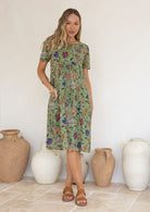 Woman wearing a green based floral print cotton dress against a white background.