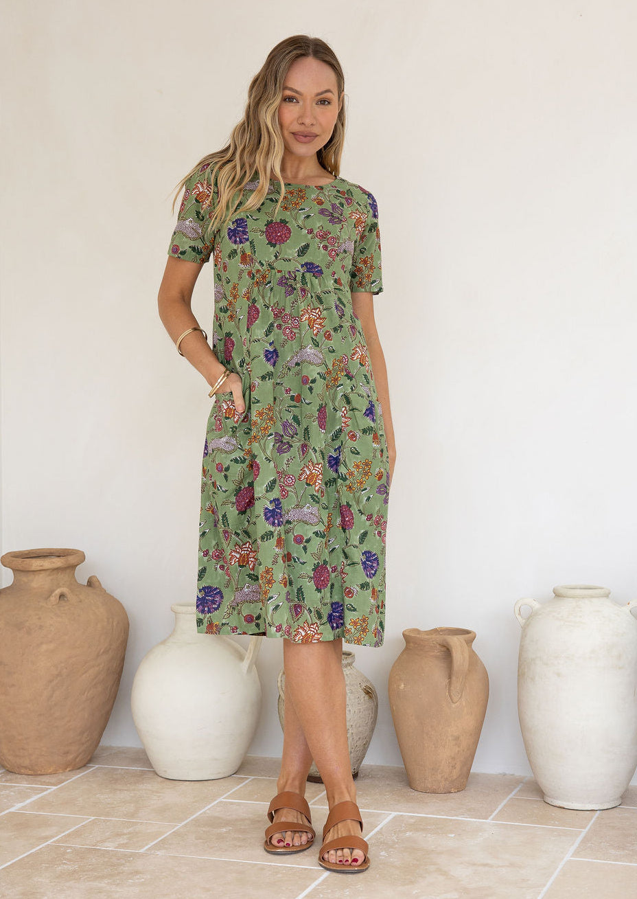 Woman wearing a green based floral print cotton dress against a white background.