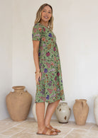 Woman wearing a green based floral print knee length cotton dress.