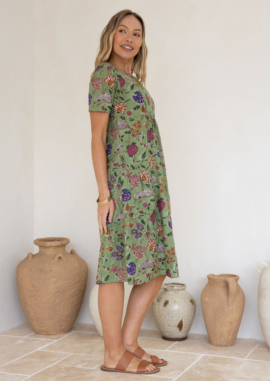Woman wearing a green based floral print knee length cotton dress.