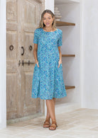 Woman wears relaxed fit 100% cotton below knee length dress with short sleeves and pockets.