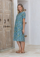 Model standing sideways in short sleeve, relaxed fit dress with deep pockets and small pin tucks at the waist.