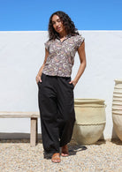 Woman with hands in pocket wears wide leg black cotton pants with elastic at either side of waist and pleated ankles