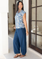 Woman stands side on wearing a dark blue 100% cotton wide leg pants with pleats at the ankles