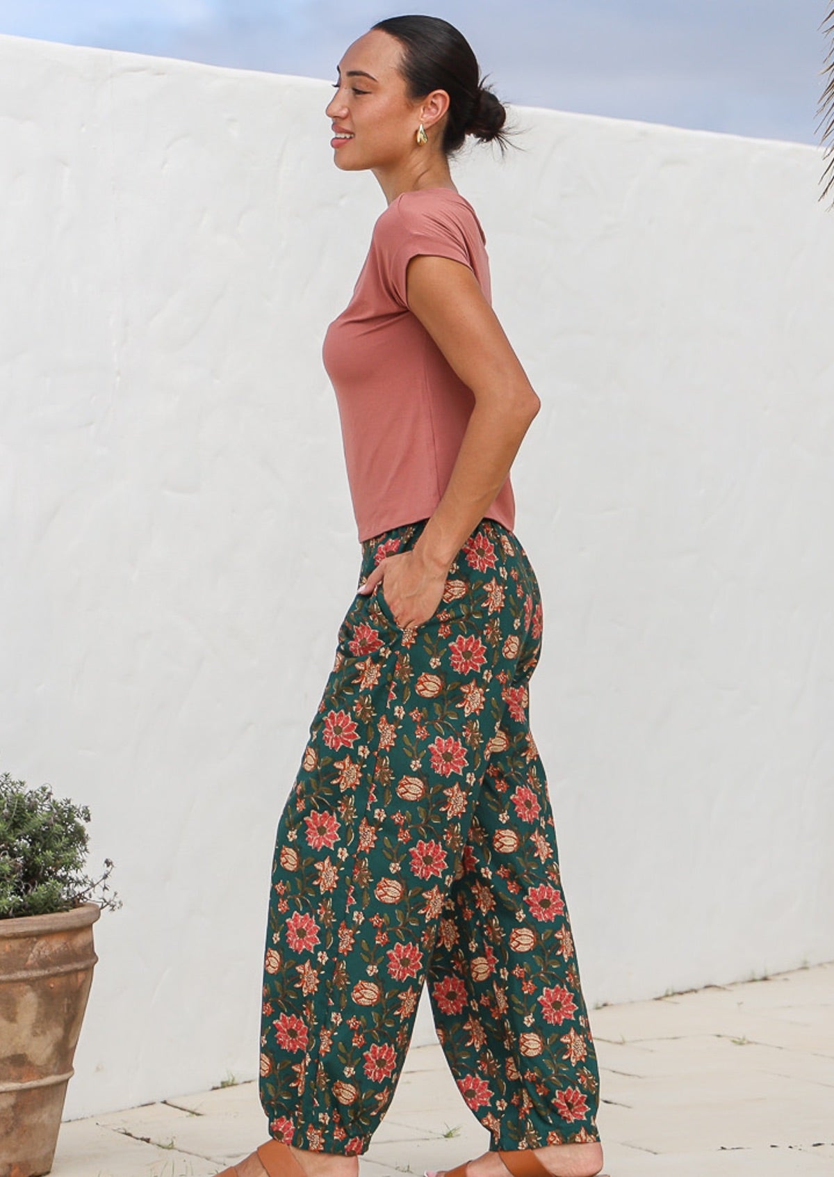 Model standing sideways with hand in pocket wearing green based floral, 100% cotton pants