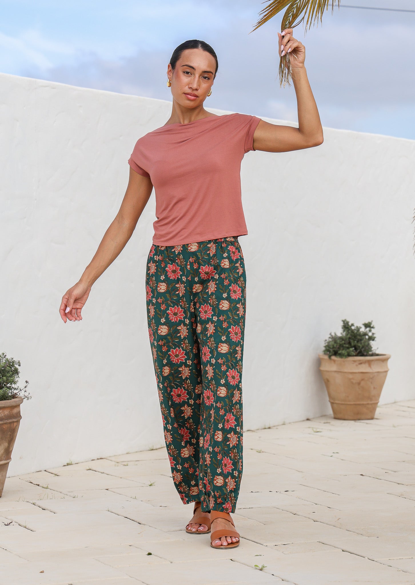 Model wears deep green based floral print cotton pants with tapered ankles, elastic waist and pockets.