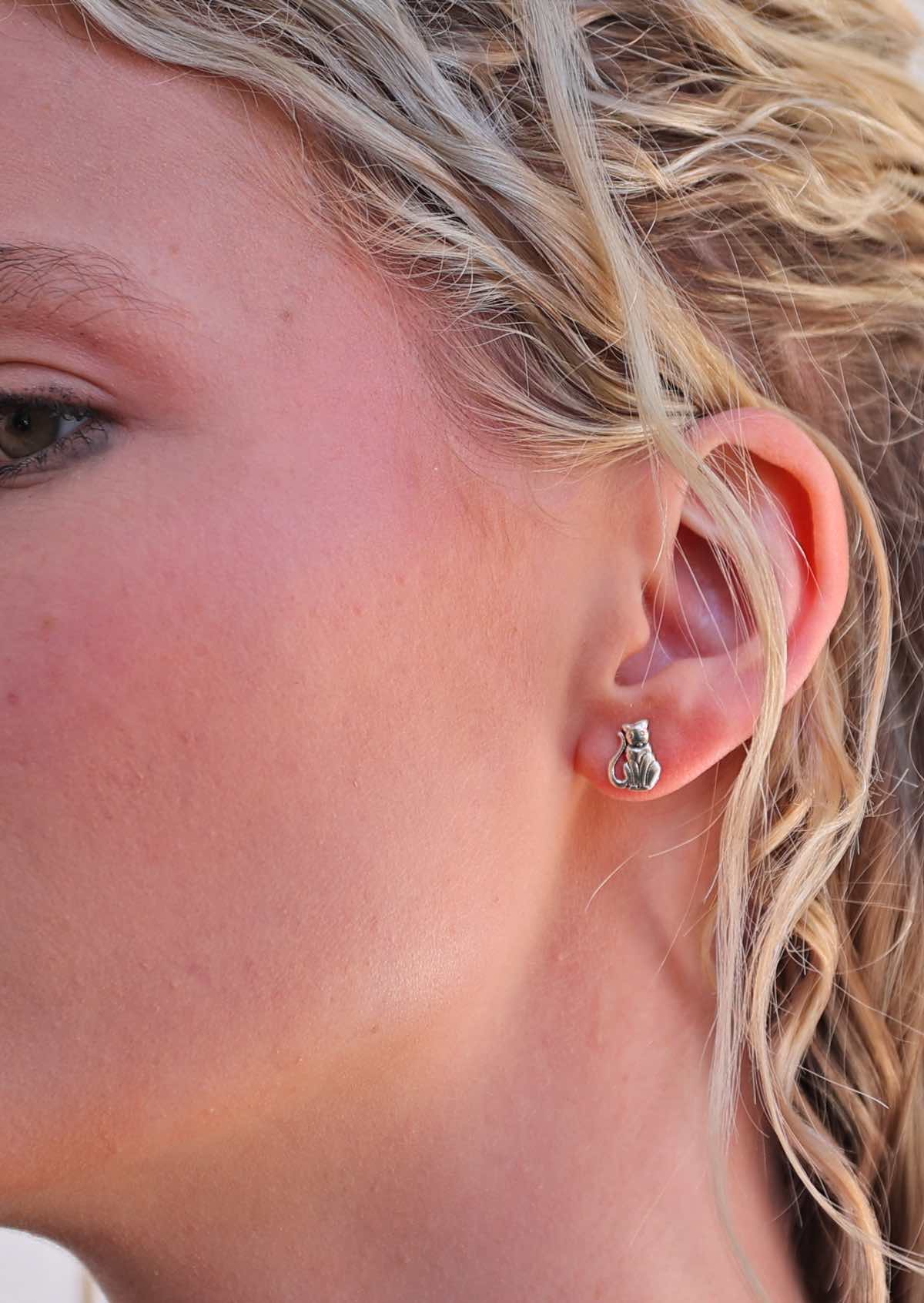 Close-up image of a woman wearing Happy Cat silver cat-shaped stud earrings.