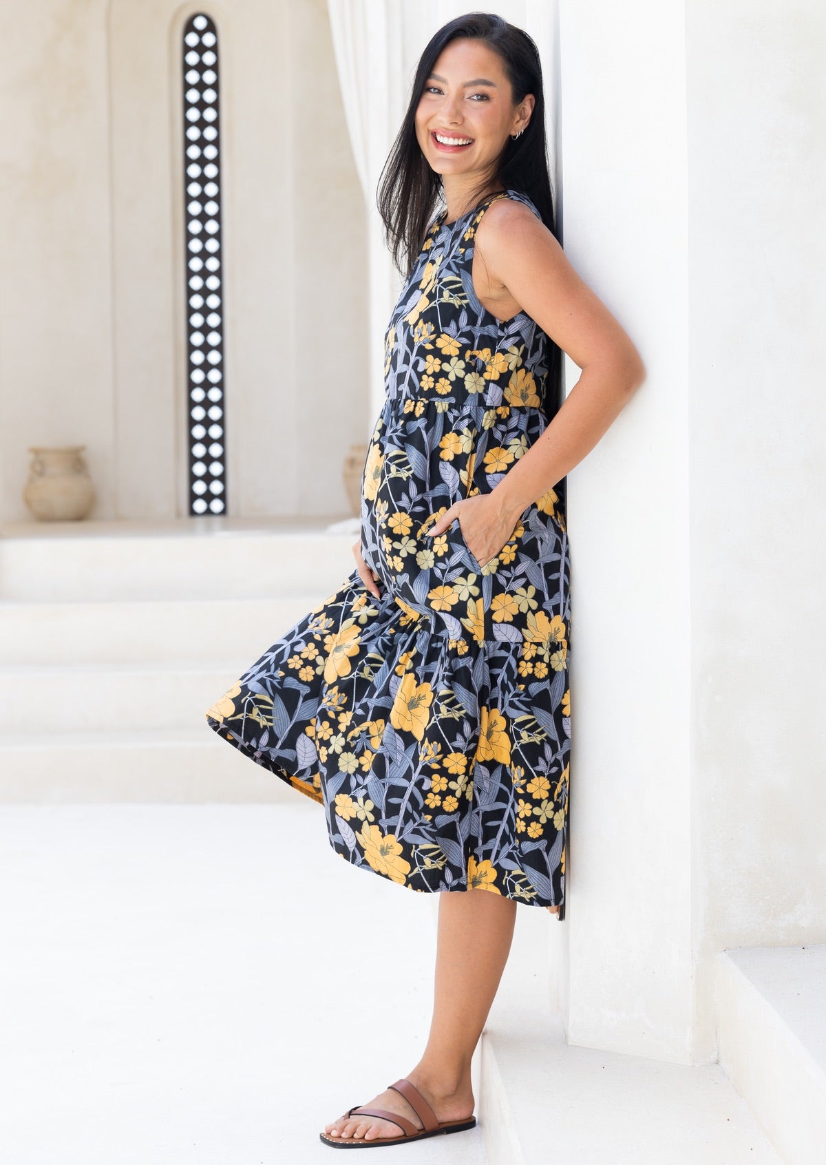 Woman stands with hand in pocket wearing a sleeveless cotton midi dress with two tiered design and high round neckline