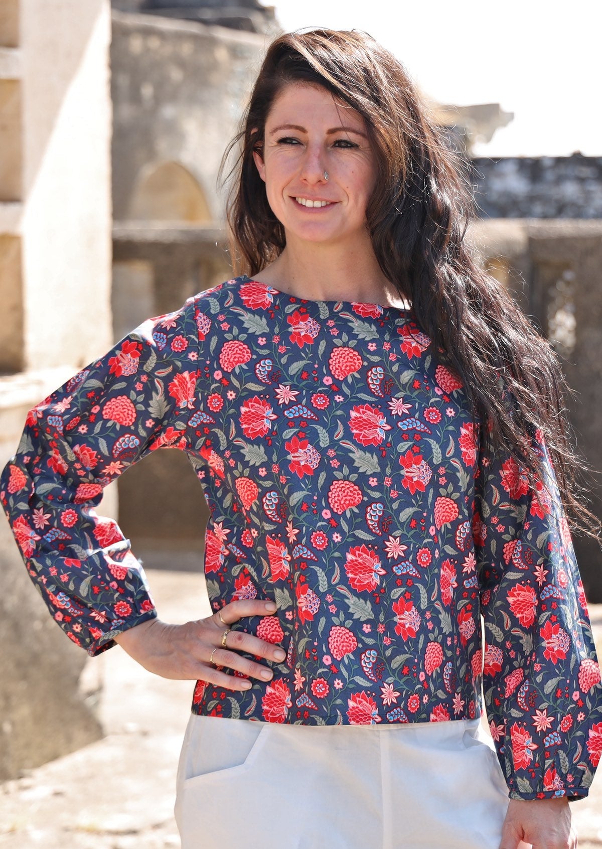Woman wears cotton top with bishop sleeves, in red and blue floral print with a boat neckline