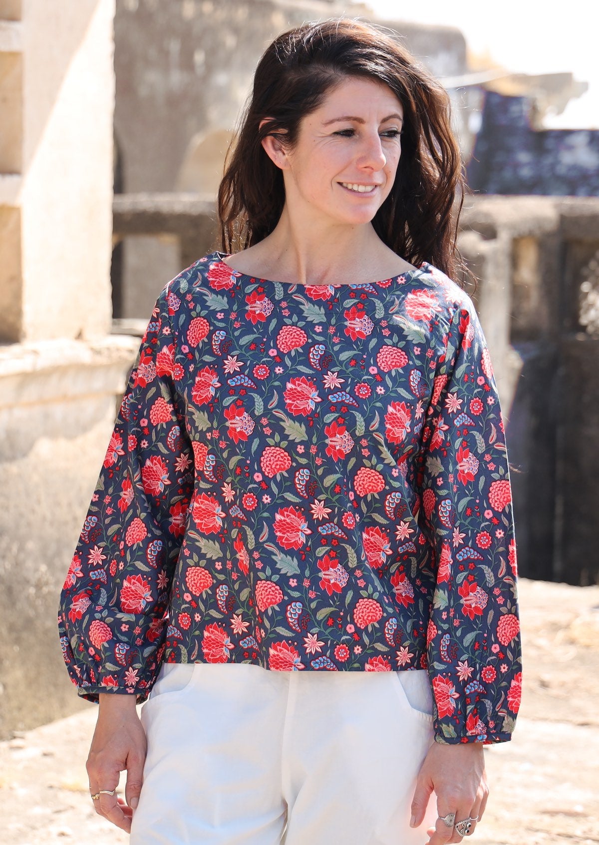 Woman wears bishop sleeve cotton top in red and blue floral print with a boat neckline