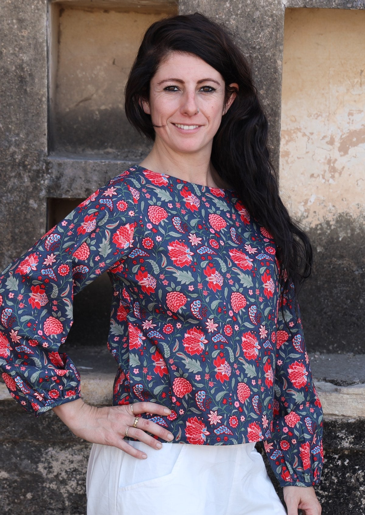 Model poses in cotton long sleeve top with boat neckline and bishop sleeves, in floral print on a blue base